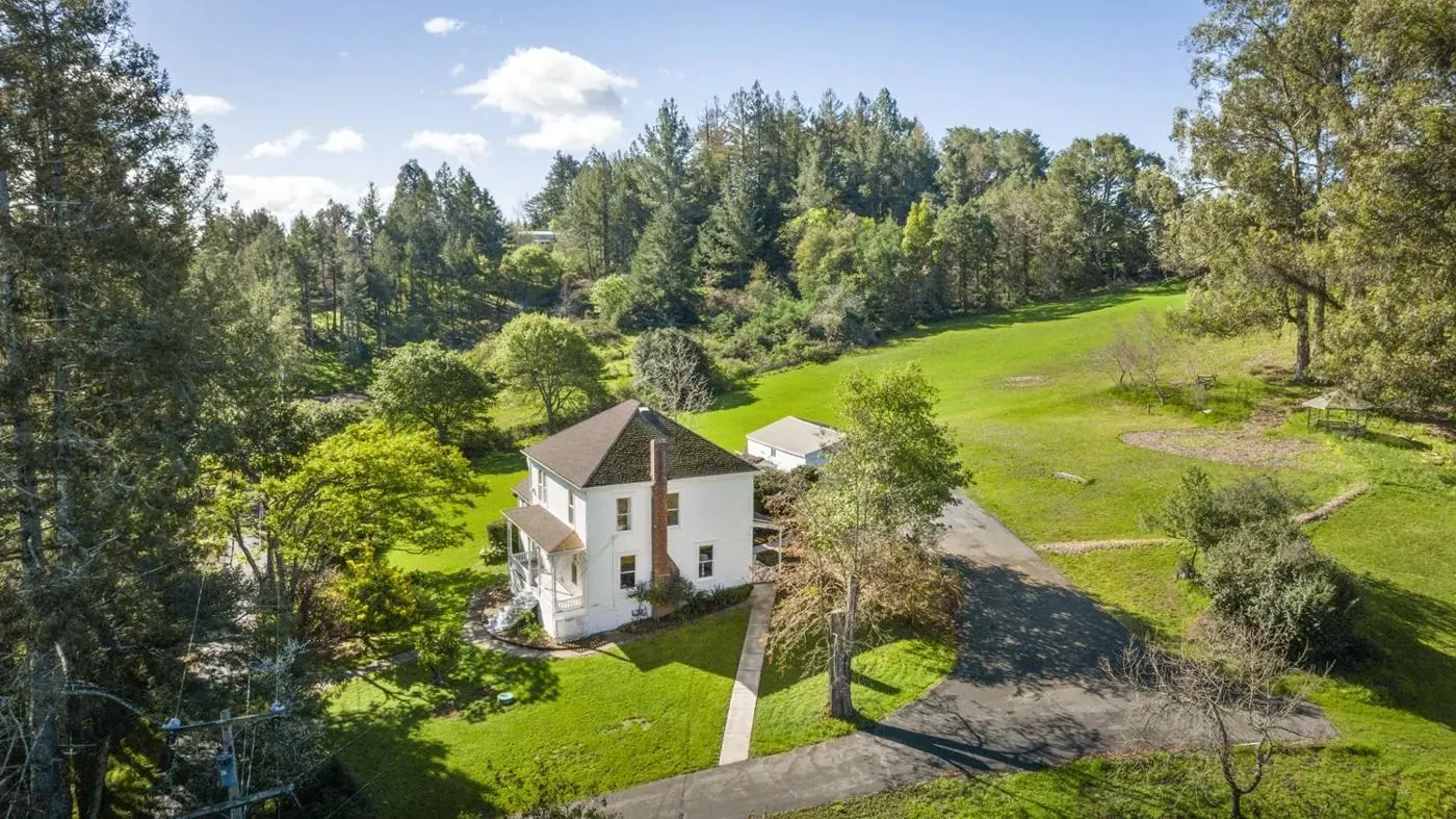 The Enos Farmhouse from above, a white 1900s farmhouse surrounded by lawn and trees