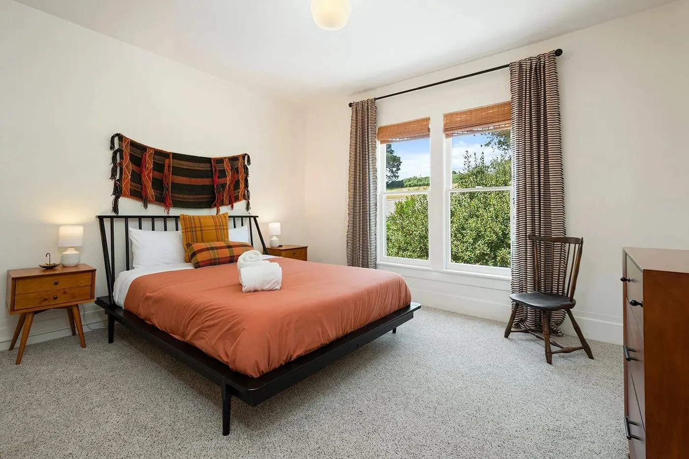 Queen bedroom with rust bedding and a woven wall hanging