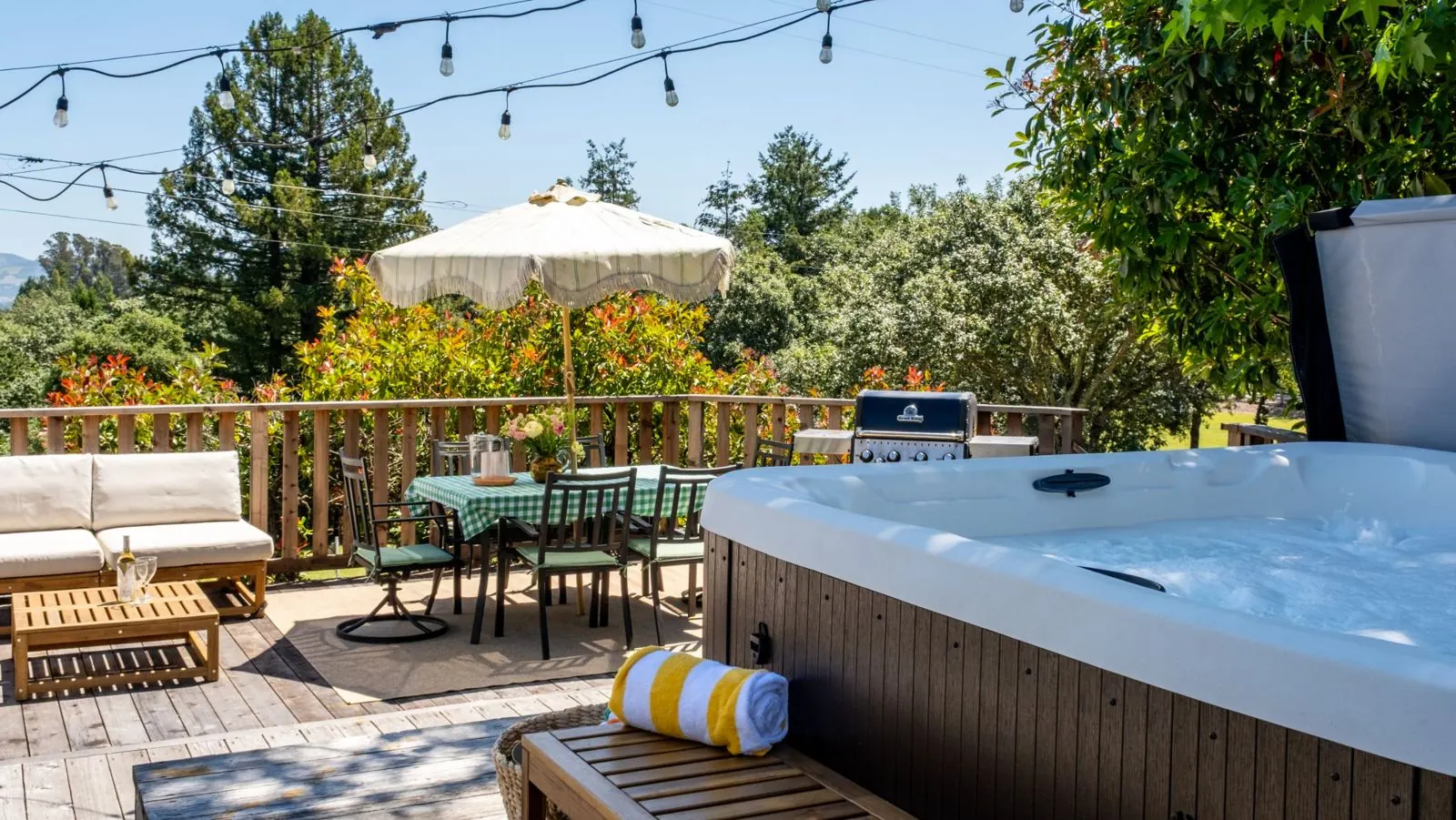 The hot tub with a striped towel on the bench, looking across the deck to the dining table and grill